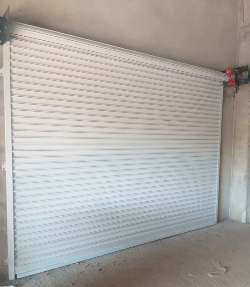 Porta de enrolar branca instalada com motor ao lado, vista por dentro